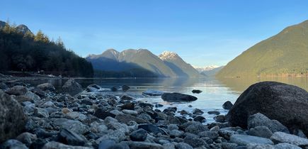 Alouette Lake bei Golden. Kleine Felssteine ragen in den See, zu sehen die schneebeckten Rocky Mountains im Hintergrund und Bäume.