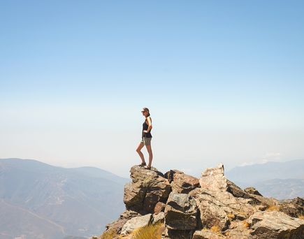 Eine Frau steht auf dem Gipfel und blickt auf den Horizont