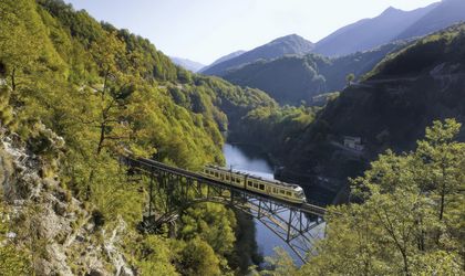 Zug fährt auf einer Brücke durch eine bergige Landschaft mit grüner Natur