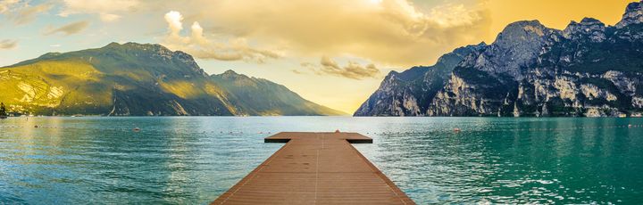 Eine Holzbrücke, die in einen See oder Fluss führt, mit Bergen im Hintergrund.