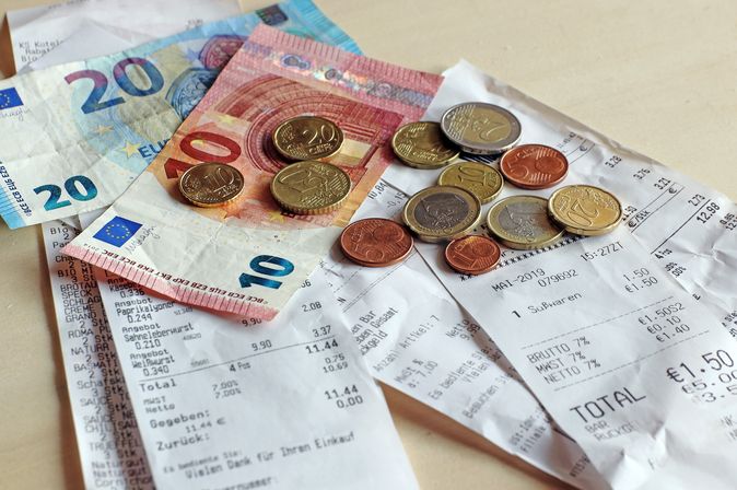 Verschiedene Münzen und Banknoten liegen auf einem Tisch, daneben ein Smartphone.