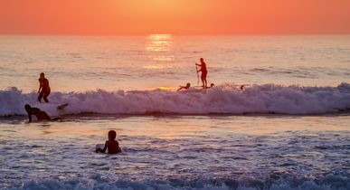 Eine Person surft bei Sonnenuntergang am Strand, mit Blick auf das Meer.