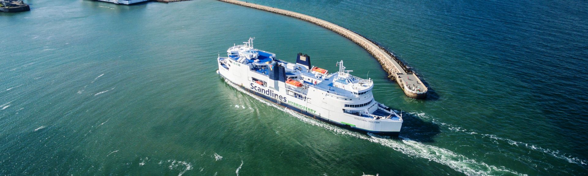 Ein großes Schiff mit einem grünen Rumpf und der Aufschrift "Scandlines" auf der Seite ist auf dem Meer zu sehen, während es eine leichte Bugwelle erzeugt.
