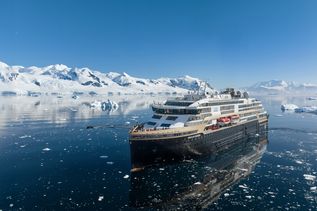 Hurtigruten Expeditions Schiff auf dem Meer mit Eisberg im Hintergrund