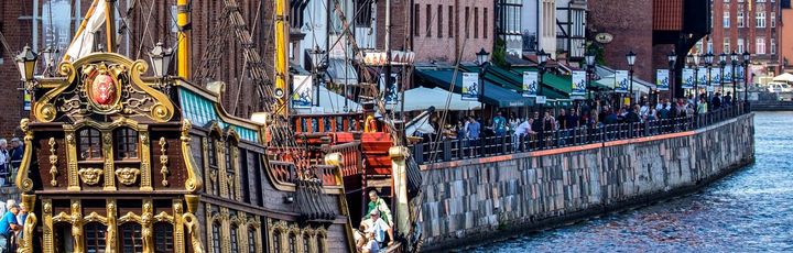 Ein historischer Kran oder eine Hebevorrichtung am Hafen, umgeben von Gebäuden.