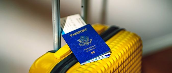Gelber Reisekoffer mit ausgezogenem Griff, darauf liegen ein blauer US-Reisepass und ein Flugticket.