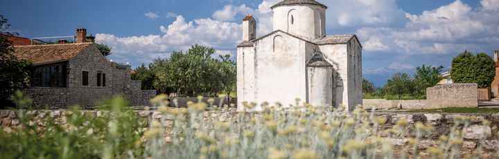 Eine historische Kirche in Nin, Kroatien, umgeben von trockener Vegetation.
