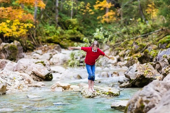 Kind geht auf Steinen über Bach