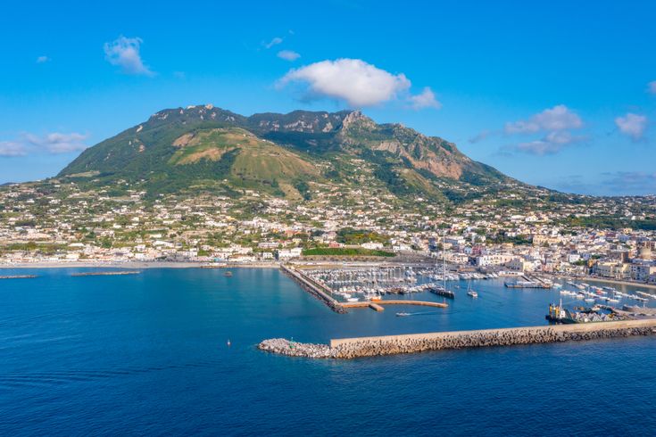 Blick aus der Vogelperspektive auf den Monte Epomeo. Davor die Stadt und davor kleine Boote im Meer.