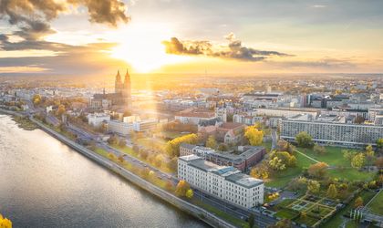 Eine Stadtansicht bei Sonnenuntergang mit einem Fluss und beleuchteten Gebäuden.