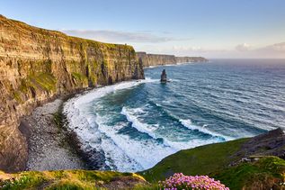 Klippen an der Küste in Irland mit Kiesstrand und aufgerautem Meer mit Wellen