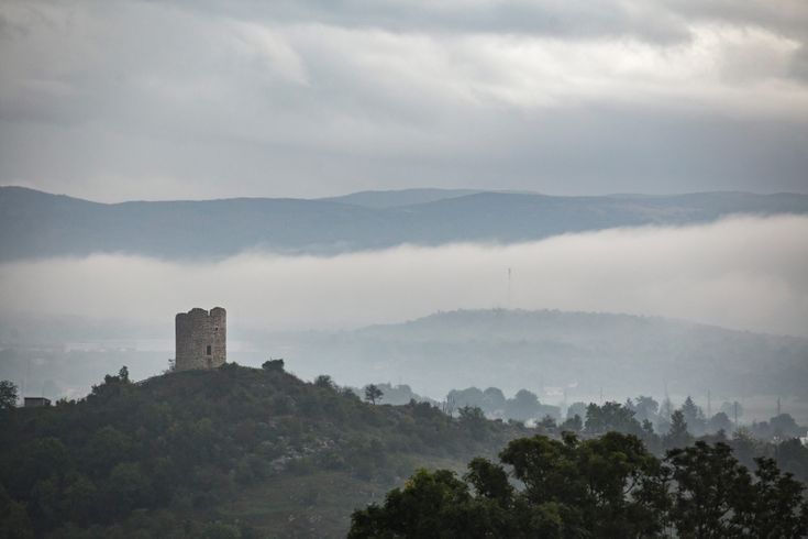 Eine alte Burgruine auf einem Hügel, umgeben von grünen Bergen.