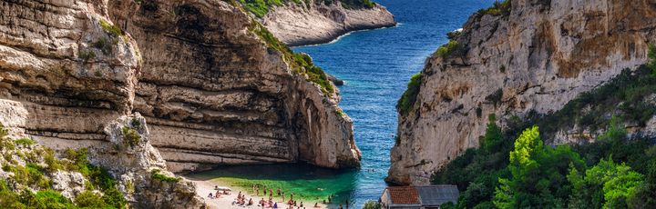 Eine felsige Bucht mit einem Strand und türkisfarbenem Wasser.