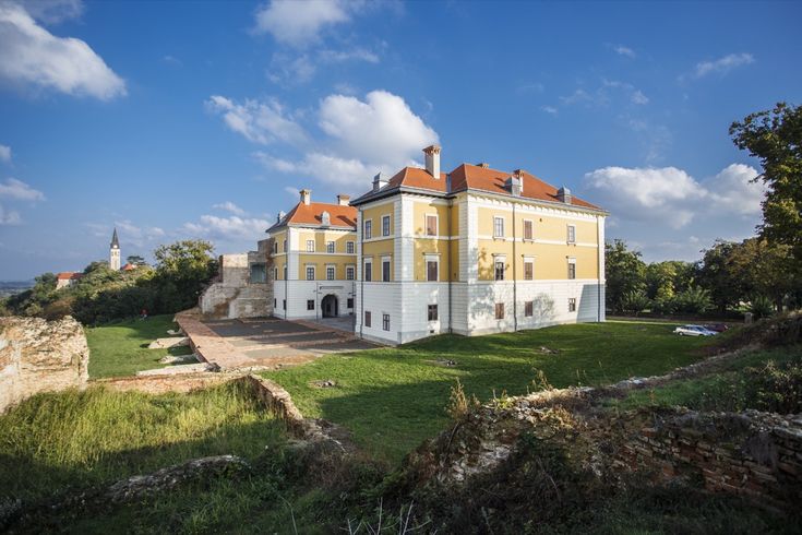 Ein Schloss oder Herrenhaus auf einem Hügel, umgeben von grüner Landschaft.