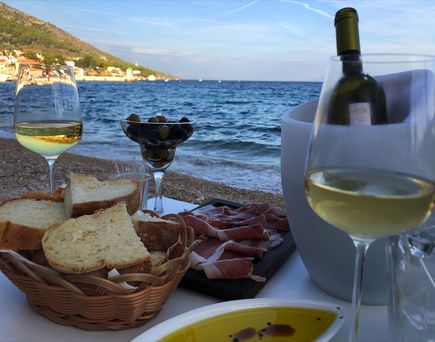 Ein Glas Weißwein und eine Platte mit Schinken am Meer.