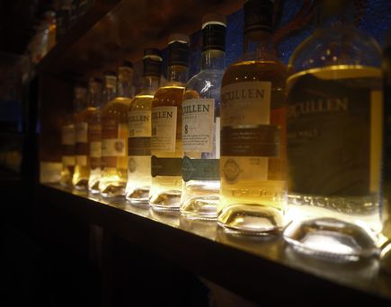 Eine Bar mit einer Reihe von beleuchteten Whiskeyflaschen, die auf einem Regal stehen. Die Flaschen sind unterschiedlich groß und geformt und zeigen verschiedene Whiskeymarken.