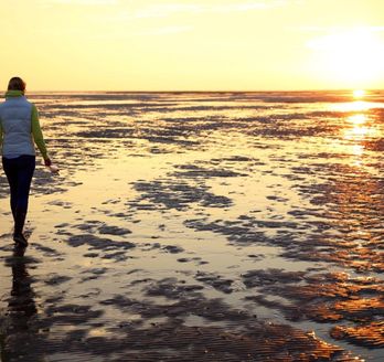 Eine Person geht auf einem Strandweg bei Sonnenuntergang.