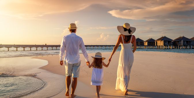 Eine Familie in den Sommerferien spaziert bei Sonnenuntergang am Strand entlang