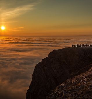 Eine Person steht auf einer felsigen Klippe und blickt auf den Sonnenuntergang über dem Meer.