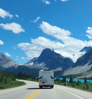 Camper fährt entlang einer Straße am Bow Lake See in Kanada. Die Straße ist umgeben von Bäumen und im Hintergrund sind Berge