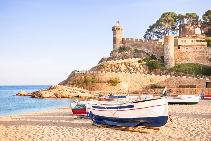 Ein Strand mit Fischerbooten und einer Burg auf einem Hügel.
