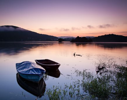 Zwei Boote liegen am Ufer des Edersees bei Sonnenuntergang, mit ruhigem Wasser und Bergen im Hintergrund.
