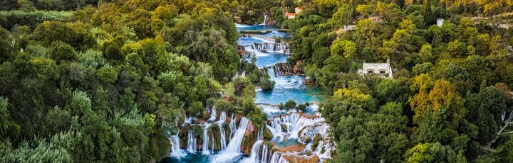 Ein Wasserfall, der in einen See fließt, umgeben von grüner Vegetation.