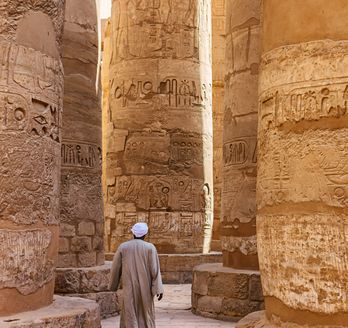 Die Säulenhalle des Karnak-Tempelkomplexes, mit hoch aufragenden, reich verzierten Säulen, die ein blau bemaltes Deckengewölbe tragen.