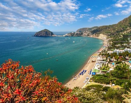 Ein Sandstrand mit blauem Meer und Felsen.