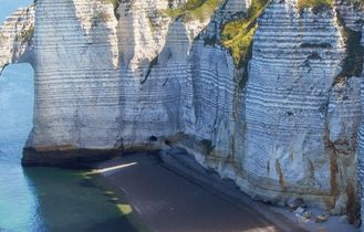 Eine felsige Küstenlinie mit hohen, weißen Klippen, die ins Meer ragen. Ein Segelboot schwimmt im türkisblauen Wasser.