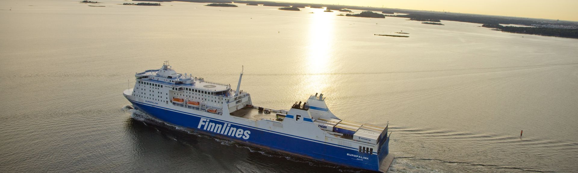Fährschiff mit der Aufschrift "FINNLINES" auf der Seite, das auf ruhigem, blauem Wasser unter einem klaren blauen Himmel fährt.