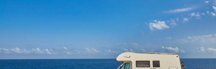 Ein Wohnmobil steht an einer trockenen Küste, das Meer und strahlend blauer Himmel im Hintergrund.