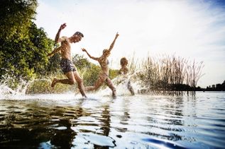 Personen, die am Seeufer ins Wasser springen oder spritzen.