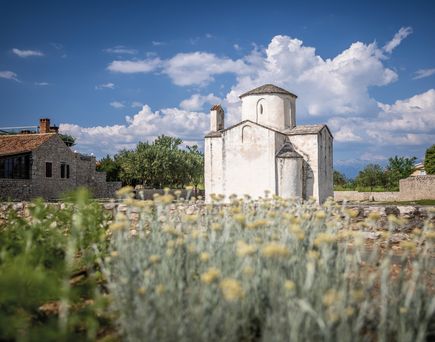 Eine historische Kirche in Nin, Kroatien, umgeben von trockener Vegetation.