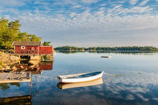 Rotes Haus in Schweden an einem See mit angelegtem Boot an einem Holzsteg und eine grüne Landzunge mit Bäumen im Hintergund