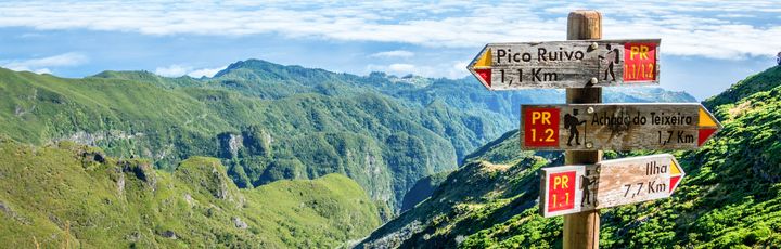 Eine grüne Berglandschaft mit einem Wanderweg und einem Wegweiser.