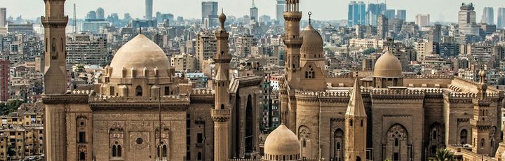 Eine Panoramansicht der Zitadelle von Kairo, mit mehreren großen Moscheen und Minaretten, die sich vor der modernen Skyline der Stadt abzeichnen.