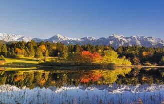 Eine Landschaft mit einem See, der sich in den Bergen spiegelt, und Bäumen in Herbstfarben.