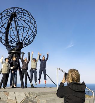 Eine Gruppe von Menschen, die vor dem Nordkap-Globusdenkmal posieren.