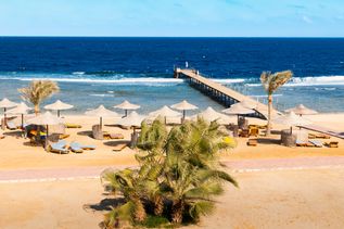 Resort am Strand mit Liegen und Sonnenschirmen und Palmen und einer Pier in Mara Alam