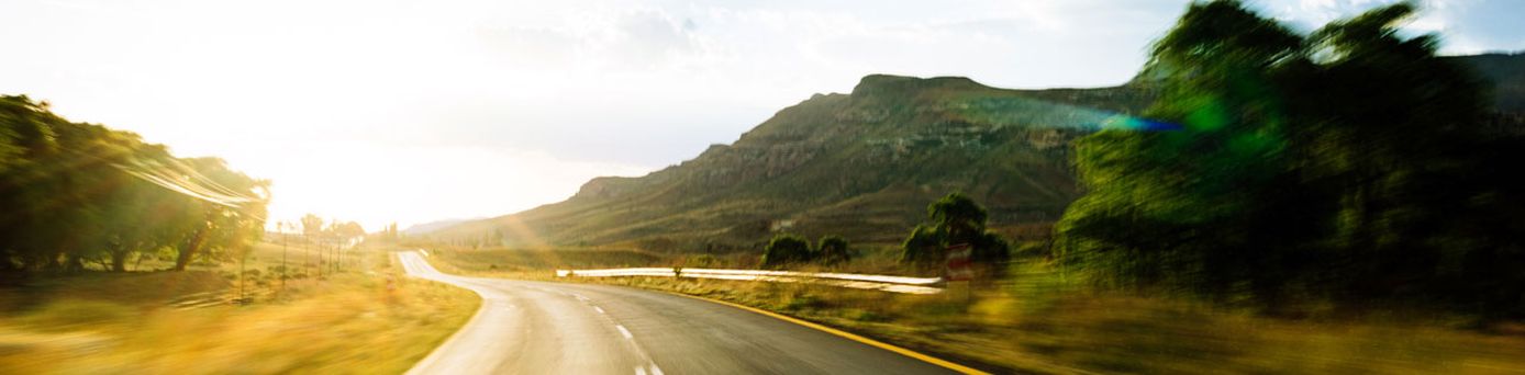 Sonnenbeschienene Landstraße in weiter Hügellandschaft – aufbruchsstarke Roadtrip-Stimmung im goldenen Licht des Morgens