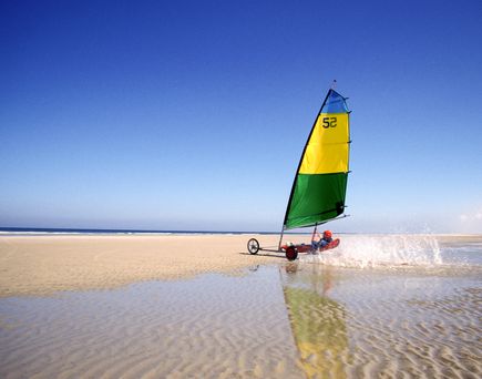 Ein Segelboot mit einem gelben Segel am Strand bei Sonnenuntergang.