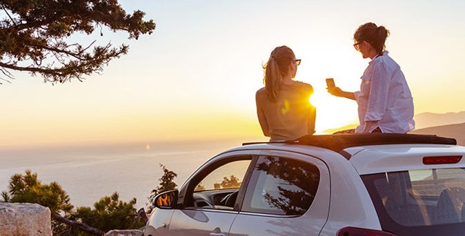 Paar sitzt auf einem Auto mit Sonnenuntergang im Hintergrund