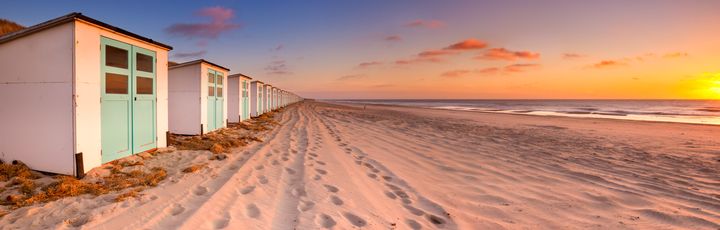 Ein weißes Holzhaus am Strand bei Sonnenuntergang.