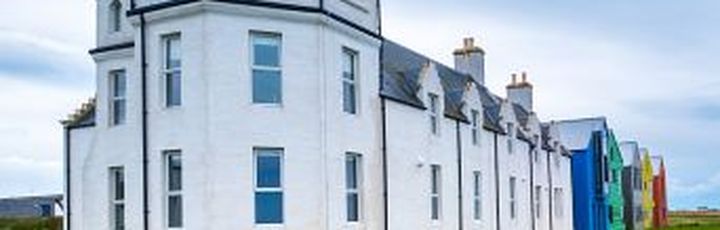 Ein weißes Schloss mit einem spitzen Turm. Das Gebäude ist von grünem Gras umgeben.