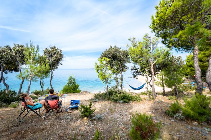 Campingplatz in Kroatien mit Zelten und Campervans am Wasser, umgeben von Bäumen.