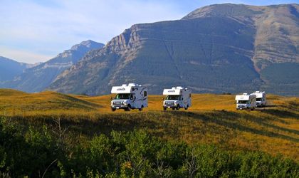 Vier Camper fahren durch einen Feld mit Gebirgen im Hintergrund
