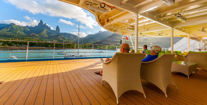 Eine Person entspannt auf einer Sonnenliege auf dem Deck eines Schiffes mit Blick auf die Landschaft.