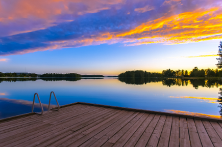 Holzsteg mit Badeleiter an einem ruhigen See unter einem farbenprächtigen Abendhimmel in Finnland.