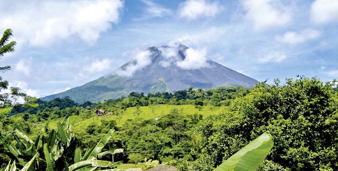 Der Vulkan Arenal in Costa Rica, umgeben von üppiger grüner Vegetation unter blauem Himmel.